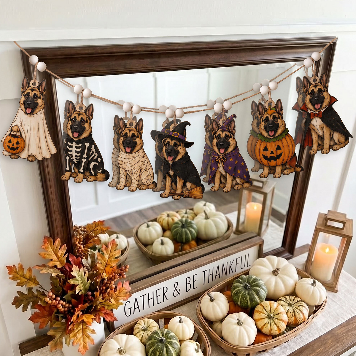 A Halloween-themed wooden dog garland with seven German Shepherd dogs dressed in costumes hangs across a large wooden mirror. The display is styled on a table with fall decorations, including a 'GATHER & BE THANKFUL' sign, pumpkins, a floral arrangement, and lanterns.