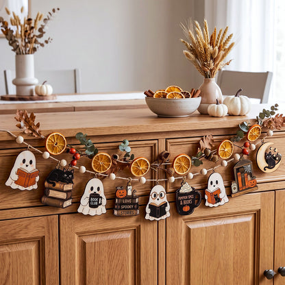 A wooden Halloween garland with ghost, pumpkin, owl, and book-themed cutouts hangs across a wooden cabinet in a warm, styled room. The scene includes dried orange slices, small pumpkins, and decorative vases in the background.