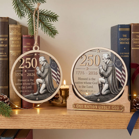 Two round wooden Christmas ornaments displayed on a wooden shelf, one hanging and one resting on a small wooden stand. The ornaments feature a silver-toned relief of a kneeling patriotic figure with an American flag background and the text '250 1776-2026 Blessed is the nation whose God is the Lord.