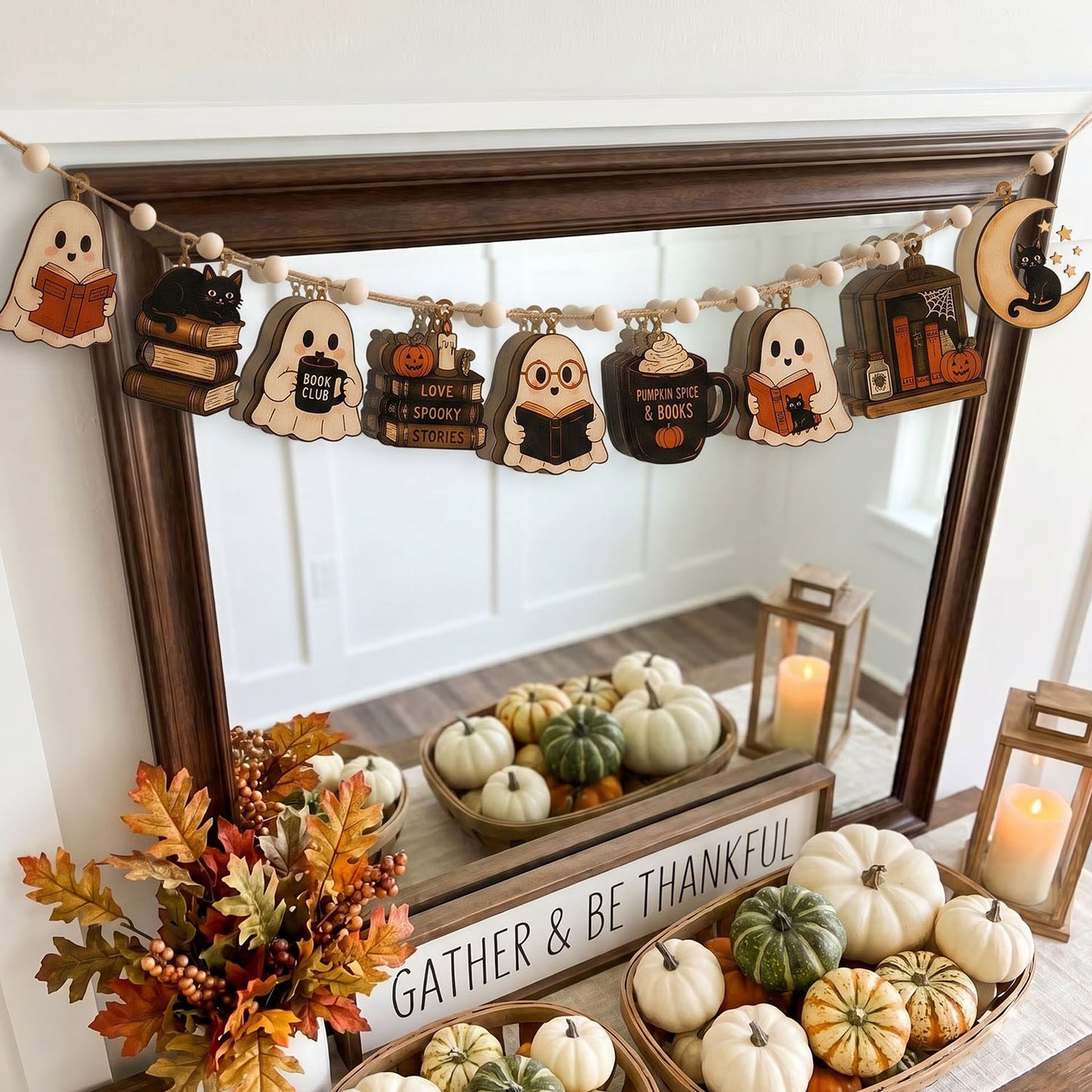 A wooden Halloween garland banner with cute ghost, cat, pumpkin, mug, and book characters, hanging above a mirror in a styled home decor setting with pumpkins and fall leaves.