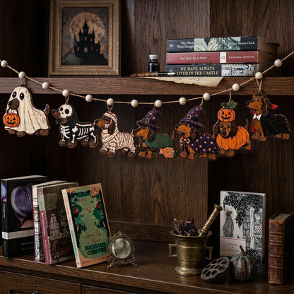 Halloween-themed wooden dog cutout garland hanging on a dark wood shelf, featuring different dog costumes including ghost, skeleton, mummy, witch, pumpkin, and vampire, styled with books and seasonal decor.