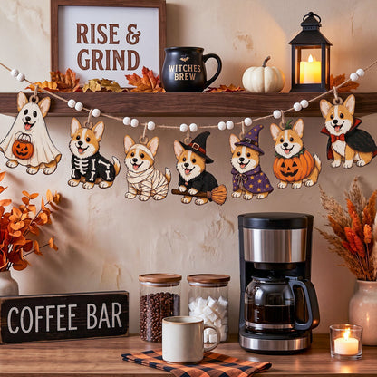 Halloween-themed wooden corgi garland with five dressed corgis hanging on a string in a cozy kitchen setting, with a coffee maker, mugs, pumpkins, and fall decor below.