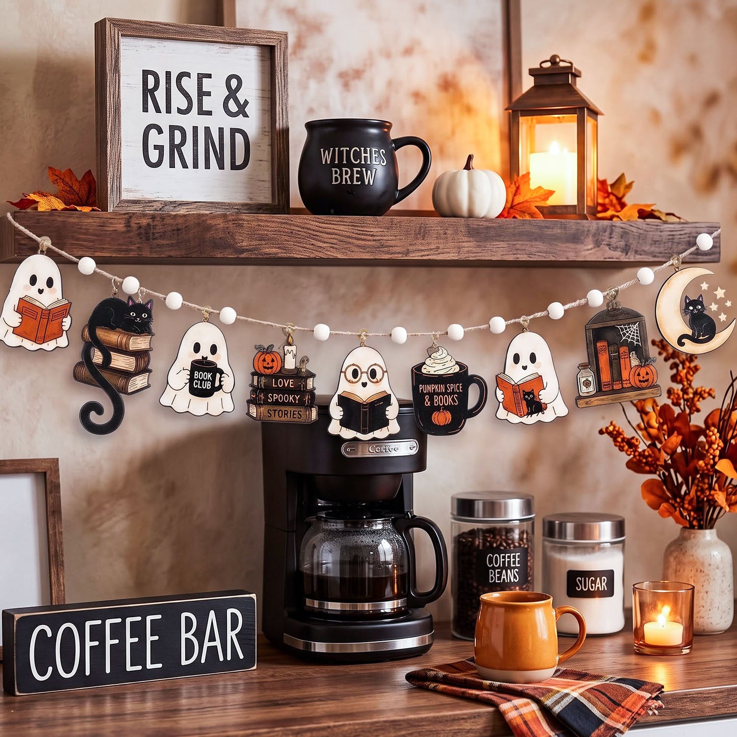 A styled autumn coffee bar shelf display with a wooden 'RISE & GRIND' sign, a black 'WITCHES BREW' mug, a lantern, fall leaves, a pumpkin, and a string banner featuring ghost, owl, pumpkin, and tombstone shapes. Below the shelf is a coffee maker, a coffee bean jar, a sugar jar, an orange mug, and a plaid napkin against a warm beige wall.