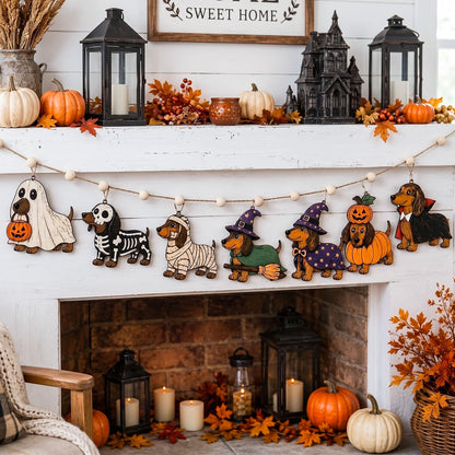 A Halloween-themed wooden dog garland with various dog costumes and accessories hangs across a white fireplace mantel, surrounded by fall decorations including pumpkins, lanterns, and autumn leaves.
