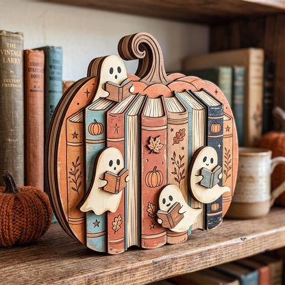 A decorative wooden pumpkin-shaped shelf piece with carved book spines and three ghost figures reading books, displayed on a rustic wooden shelf with vintage books and a mug in the background.