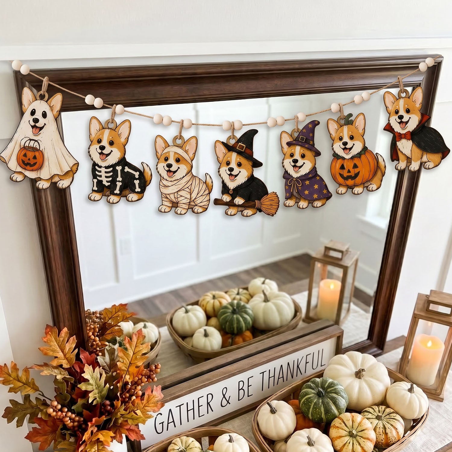 A Halloween-themed wooden dog garland with seven cutout dogs dressed in ghost, skeleton, bandage, witch, wizard, pumpkin, and vampire costumes, hanging across a dark wood mirror in a decorated fall display with pumpkins and candles.