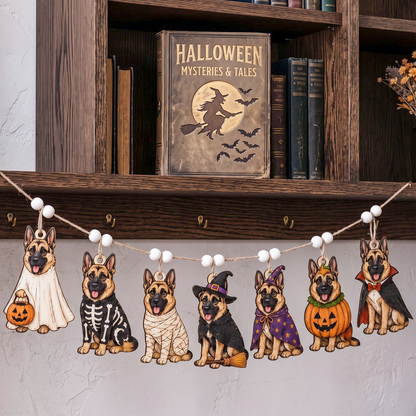 Halloween dog costume garland with six German Shepherd dog cutouts in different costumes hanging on a string with white beads, displayed in a home setting below a wooden bookshelf.