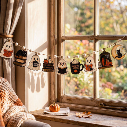 A Halloween-themed wooden garland with cute illustrations of ghosts, pumpkins, a mug, a lantern, and a crescent moon, hanging across a sunlit window above a windowsill with a small pumpkin and autumn leaves.
